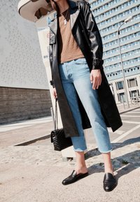 Abrigo largo de cuero negro, top marrón, vaqueros cortos azul claro, mocasines negros sin cordones y un bolso negro acolchado con cadena.