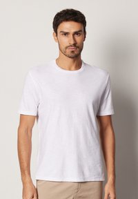 Vit kortärmad t-shirt i ett lättviktigt tyg med rund halsringning. Slät textur, avslappnad passform och subtila detaljer längs ärmarna.