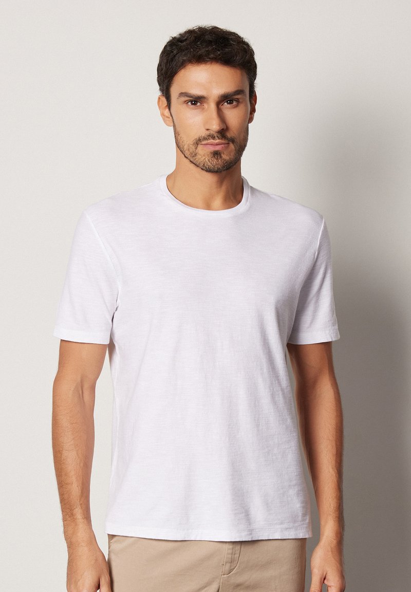 Vit kortärmad t-shirt i ett lättviktigt tyg med rund halsringning. Slät textur, avslappnad passform och subtila detaljer längs ärmarna.