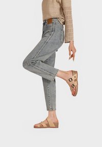 Sandali beige con due cinghie regolabili, suola in sughero e parte superiore testurizzata. Indossati con jeans a sigaretta azzurri chiari e un top in maglia beige.