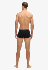 Boxer-briefs noirs au design ajusté, dotés d'une ceinture élastique grise avec le logo "SUPERDRY". Le matériau semble lisse et doux.