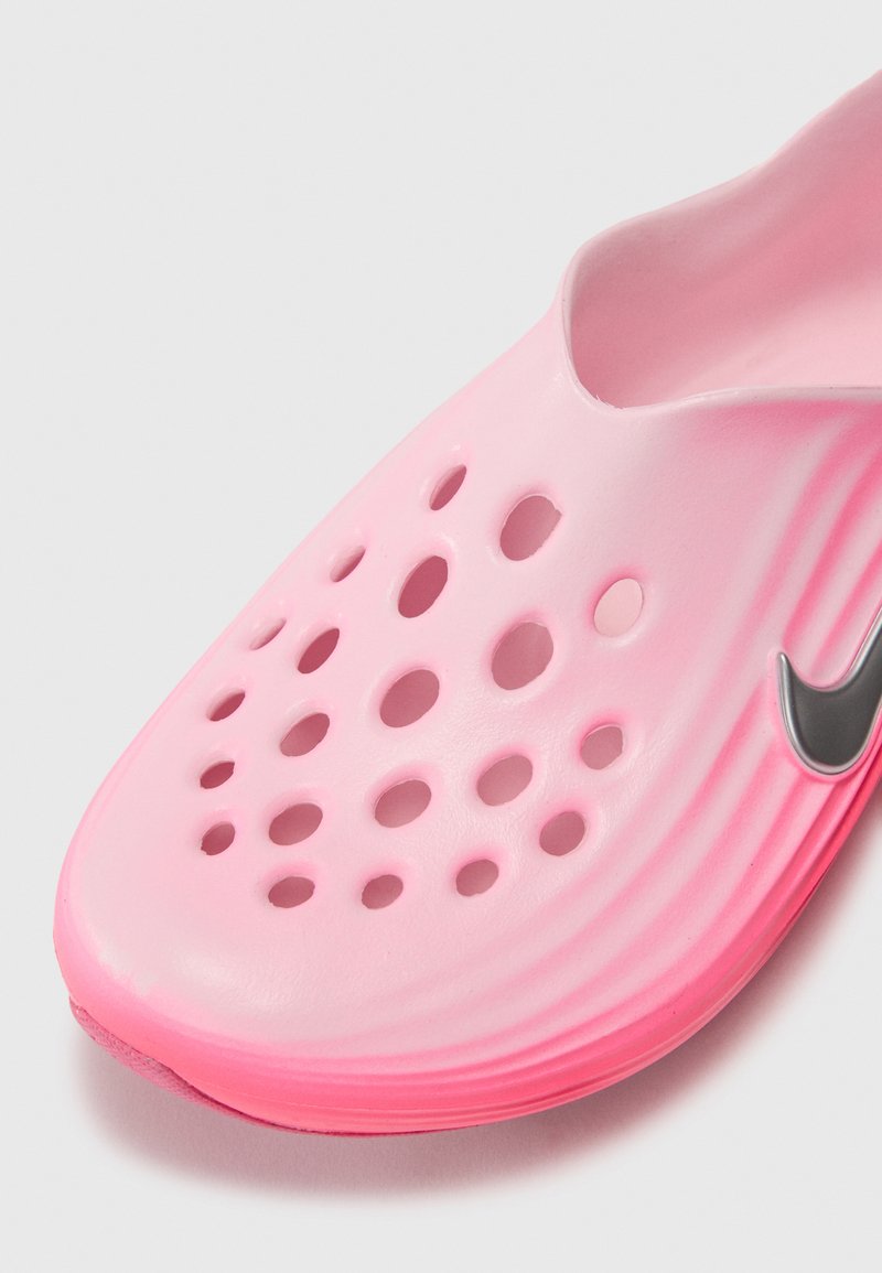 Zapato slip-on rosa hecho de material ligero con diseño perforado. Presenta una textura suave y un acento del logo de Nike en color gris.