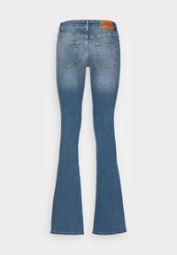 Modré rozšírené džínsy z denimu s dvoma zadnými vreckami, stredne vysokým pásom a hnedou logo nášivkou na zadnej strane pásu.