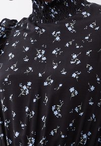 Robe en tissu noir avec un motif floral présentant des fleurs bleu clair. Elle a un col smocké et des manches froncées, créant texture et détail.