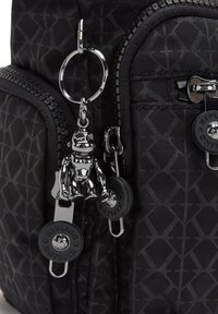 Schwarzer Stoffrucksack mit geometrischem Muster, zwei Reißverschlusstaschen und einem silbernen Affen-Schlüsselanhänger, der an einem Reißverschluss befestigt ist.