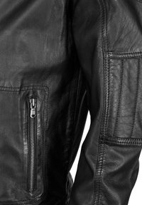 Schwarze Lederjacke mit einer Reißverschlusstasche am Arm, strukturiertem Finish und sichtbaren Steppnähten entlang der Nähte.