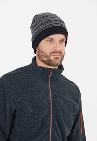 Sort og grå stribet hue med ribbet kant, båret med en mørk struktureret zip-up jakke med røde accenter og lomme på armen.