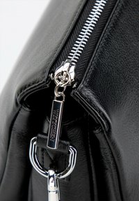 Narożnik czarnej skórzanej torby z srebrnym zamkiem błyskawicznym i uchwytem. Zamek ozdobiony jest metalowym akcentem z napisem "WITTCHEN".
