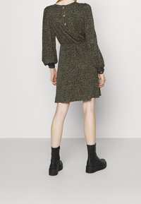 Robe verte avec imprimé léopard noir, manches longues, poignets élastiques et détail de boutons au dos. Associée à des bottines noires.