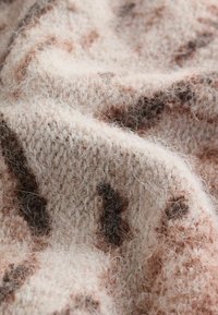Tejido de punto en rosa pálido con manchas marrones oscuras, que presenta una textura suave y esponjosa y un diseño de tejido suelto. Fibras que captan la luz visibles.