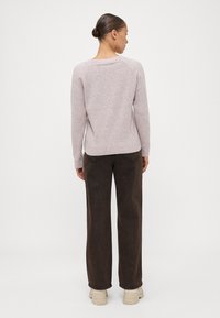 Sweater de malha rosa claro com um corte solto e punhos canelados, combinado com calças largas castanho-escuro e ténis bege. Design simples e texturizado.