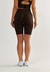 Brązowe rowerowe szorty prążkowane z wysokim stanem, teksturowana tkanina i dopasowany krój, w połączeniu z białymi butami sportowymi.