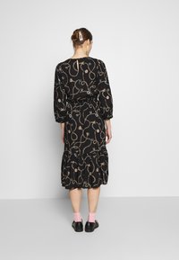 Svart klänning med guldchain och accessoartryck, elastisk midja, puffärmar och en lagd fåll. Stylad med svarta skor och rosa strumpor.