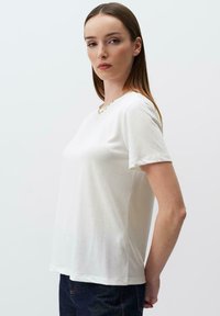 T-shirt bianco a maniche corte realizzato in tessuto morbido. Presenta un neckline rotondo e una vestibilità rilassata, con una texture liscia e un design minimalista.