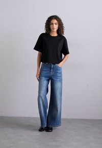 Juodas trumpas marškinėliai su trumpomis rankovėmis, derinami su aukštu liemeniu, plačiomis mėlynomis džinsinėmis kelnėmis; lygus paviršius, su šoninėmis kišenėmis ir minimaliais siūlės.