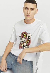 Hvid T-shirt med korte ærmer, der har et grafisk tryk af tre kranier og roser i rød og grøn. Lavet af bomuld med en regular fit.