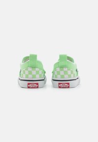 Zapatos verdes tipo slip-on con un patrón de cuadros, hechos de lona. Cuenta con una suela de goma y un logo rojo "VANS OFF THE WALL" en el talón.