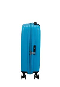 Valigia rigida blu con superficie testurizzata, tre ruote, una maniglia laterale e serratura combinata. Forma compatta e rettangolare.