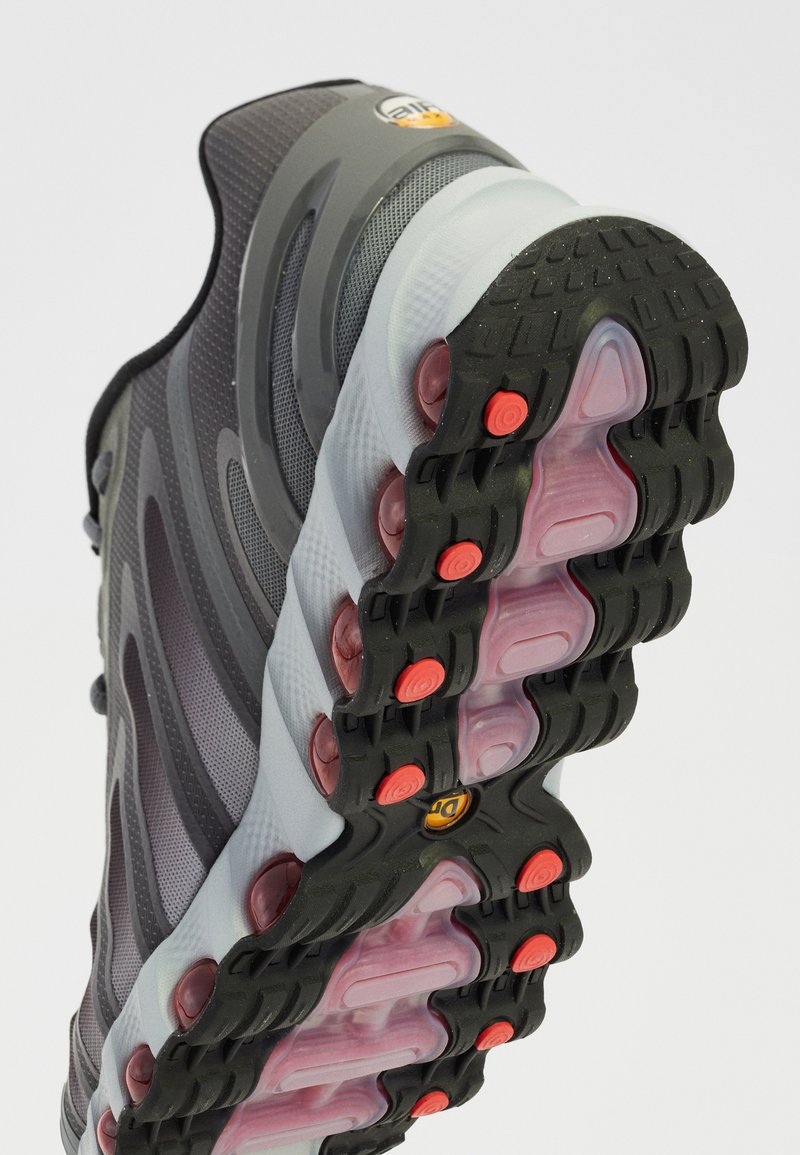 Zapatilla deportiva gris con un upper texturizado, diseño en capas y una suela de goma con acentos de color y cápsulas de amortiguación.