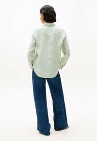 Camicia a righe verde chiaro con colletto classico, maniche lunghe, orlo arrotondato, abbinata a jeans blu in denim a gamba larga.