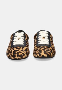 Zapatos tipo slip-on con estampado de leopardo, lazadas blancas planas, detalles de cuero negro, puntera redondeada y superficie texturizada.