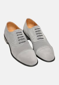 Chaussures habillées en suede gris avec une finition lisse, présentant un design à bout cap, six œillets noirs et une semelle noire élégante.