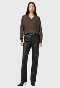 Maglione verde oliva a scollo a v con vestibilità rilassata, pantaloni in pelle nera a gamba dritta e tacchi a punta neri. Una semplice cintura con fibbia aggiunge un tocco di dettaglio.