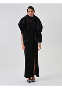 Robe de soirée noire avec une fente haute sur la cuisse, accompagnée d'un châle en fausse fourrure noire. Des talons scintillants noirs et argent complètent la tenue.