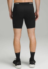 Sorte atletiske shorts lavet af et glat, strækbart stof. Har en refleksstribe i taljen og kontrasterende søm detaljer.