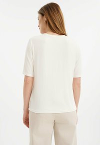 Korte mouwen, crèmekleurige top van zachte stof, met een ronde halslijn en rechte zoom, gecombineerd met licht beige broeken.