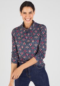 Maglietta a maniche lunghe blu navy con un motivo floreale in rosa, crema e rosso, dotata di colletto e dettagli arricciati sullo scollo.