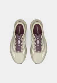 Μπεζ αθλητικά παπούτσια με μωβ κορδόνια και λεπτομέρειες, με υφασμένο άνω μέρος, καμπυλωτή σόλα και τρεις λευκές πλευρικές ρίγες.