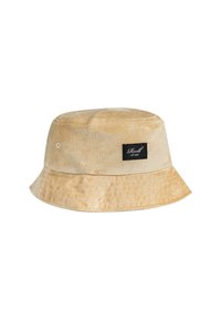 Beige Bucket Hat aus weichem Stoff, ausgestattet mit einem schwarzen Etikett und weißem Text. Der Rand ist breit und flach mit einer strukturierten Oberfläche.