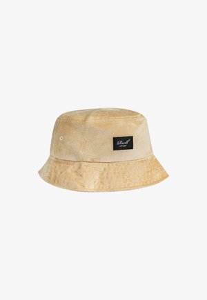 Beige bucket hat made of soft fabric, featuring a black label with white text. The brim is wide and flat, with a textured surface.