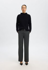 Schwarzer gerippter Pullover mit hohem Kragen, kombiniert mit grauen, taillierten Hosen und schwarzen spitzen High Heels, ausgestattet mit einem Gürtel und minimalistischen Design.