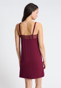 Burgundowa nocna koszula uszyta z miękkiego materiału, z regulowanymi ramiączkami i koronkowym wykończeniem na plecach, do kolan, o luźnym kroju.