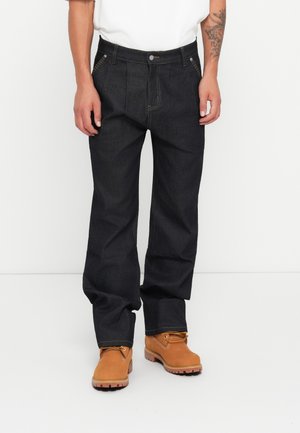 Donkerblauwe denim jeans met een ontspannen pasvorm, zichtbare stikdetails en twee voorkruiszakken. Gecombineerd met tan werklaarzen.