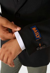 Melna žakete ar baltām piedurknēm. Ievērojams zils uzlīmes teksts "DAILY" oranžā krāsā, kā arī melni pogas ar oranžiem šuvumiem.