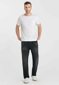 T-shirt blanche à col rond avec une poche sur la poitrine, associée à un jean gris foncé. La tenue est complétée par des baskets blanches et un design simple.