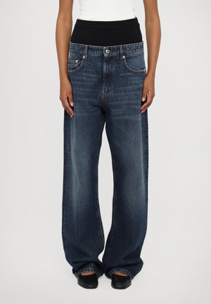 Jeans in denim scuro a gamba larga con una cintura a costine nera e tasche posteriori. Presentano una texture scolorita e leggero strappo sul tessuto.