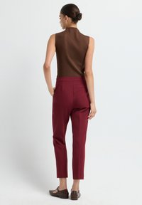 Bruine mouwloze top, aansluitende vorm, geribbeld textuur; gecombineerd met hoog- taille, taps toelopende bordeauxrode broek en bruine platte schoenen met een textuurpatroon.