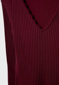 Haut en ribologia bourgogne avec décolleté en V, présentant des lignes verticales, un tissu texturé et des finitions brutes le long du décolleté pour un détail supplémentaire.