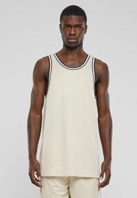 Tank topp i beige mesh-stoff med svart og hvit stripete kant ved halslinningen. Løs passform med rett falm. Ingen synlige mønstre eller grafikk.