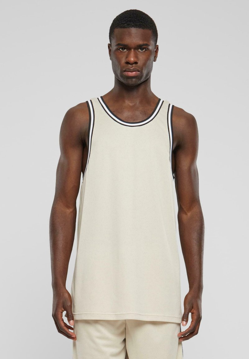 Tank topp i beige mesh-stoff med svart og hvit stripete kant ved halslinningen. Løs passform med rett falm. Ingen synlige mønstre eller grafikk.