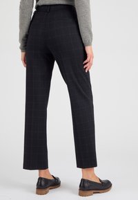 Zwarte geruite broek met een recht model, gemaakt van een glad materiaal, met achterzakken en gecombineerd met zwarte loafers.