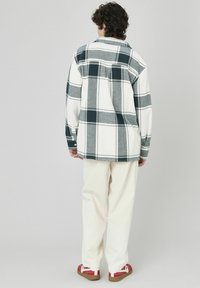 Chemise à boutons en motif vichy blanc et gris, avec des manches longues et une coupe décontractée, associée à un pantalon écru et des chaussures à motif rouge.