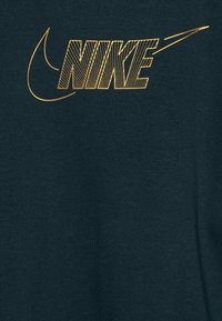 Dunkelgrüner Stoff mit einem goldenen Nike-Logo, geprägt von kräftiger Typografie und diagonalen Linienmustern für Textur.