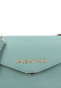 Sac à main en cuir bleu clair avec un logo doré "VALENTINO", fermé par un rabat et présentant des détails de couture.