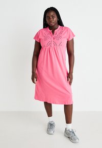 Vestido de algodão rosa com decote tipo henley e mangas curtas. Apresenta padrões decorativos recortados no corpete. Design até ao joelho.