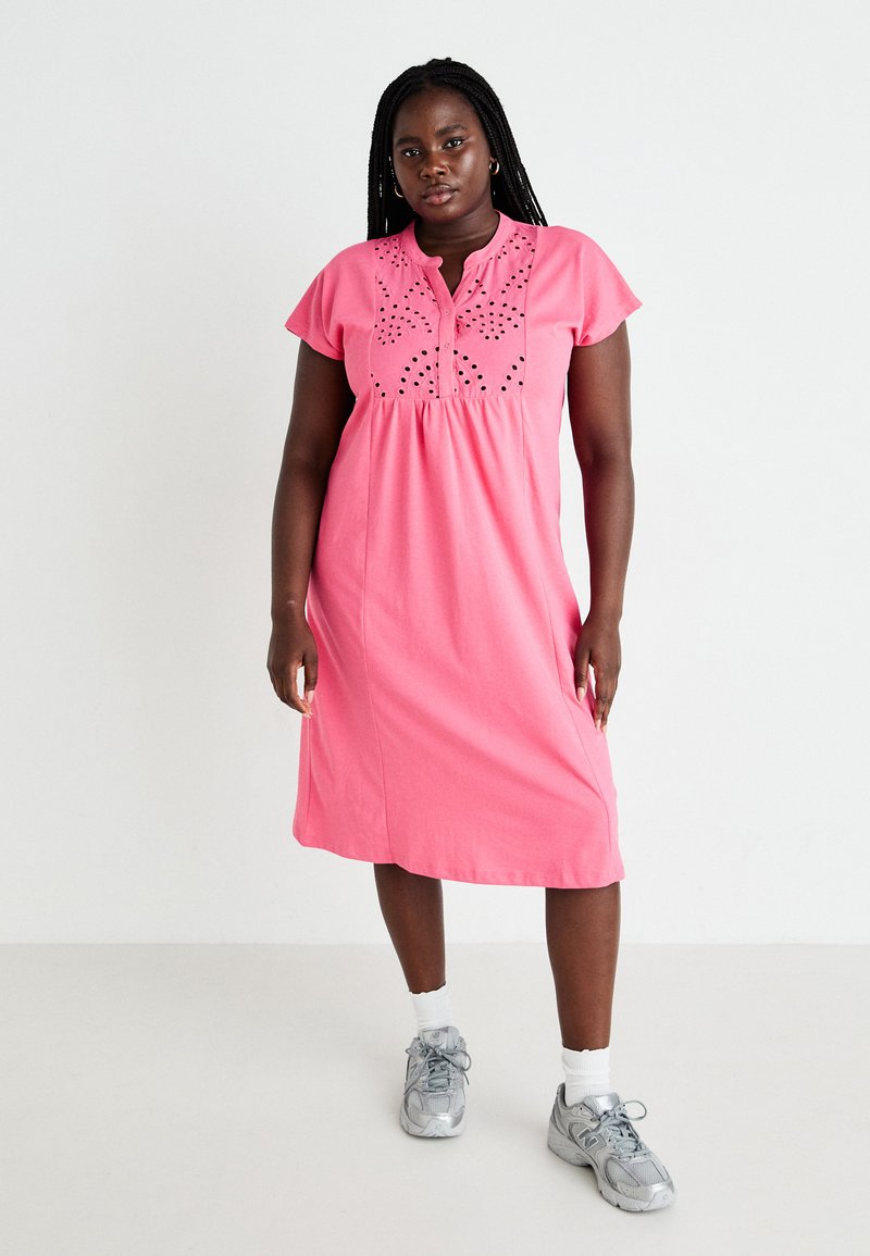 Vestido de algodão rosa com decote tipo henley e mangas curtas. Apresenta padrões decorativos recortados no corpete. Design até ao joelho.